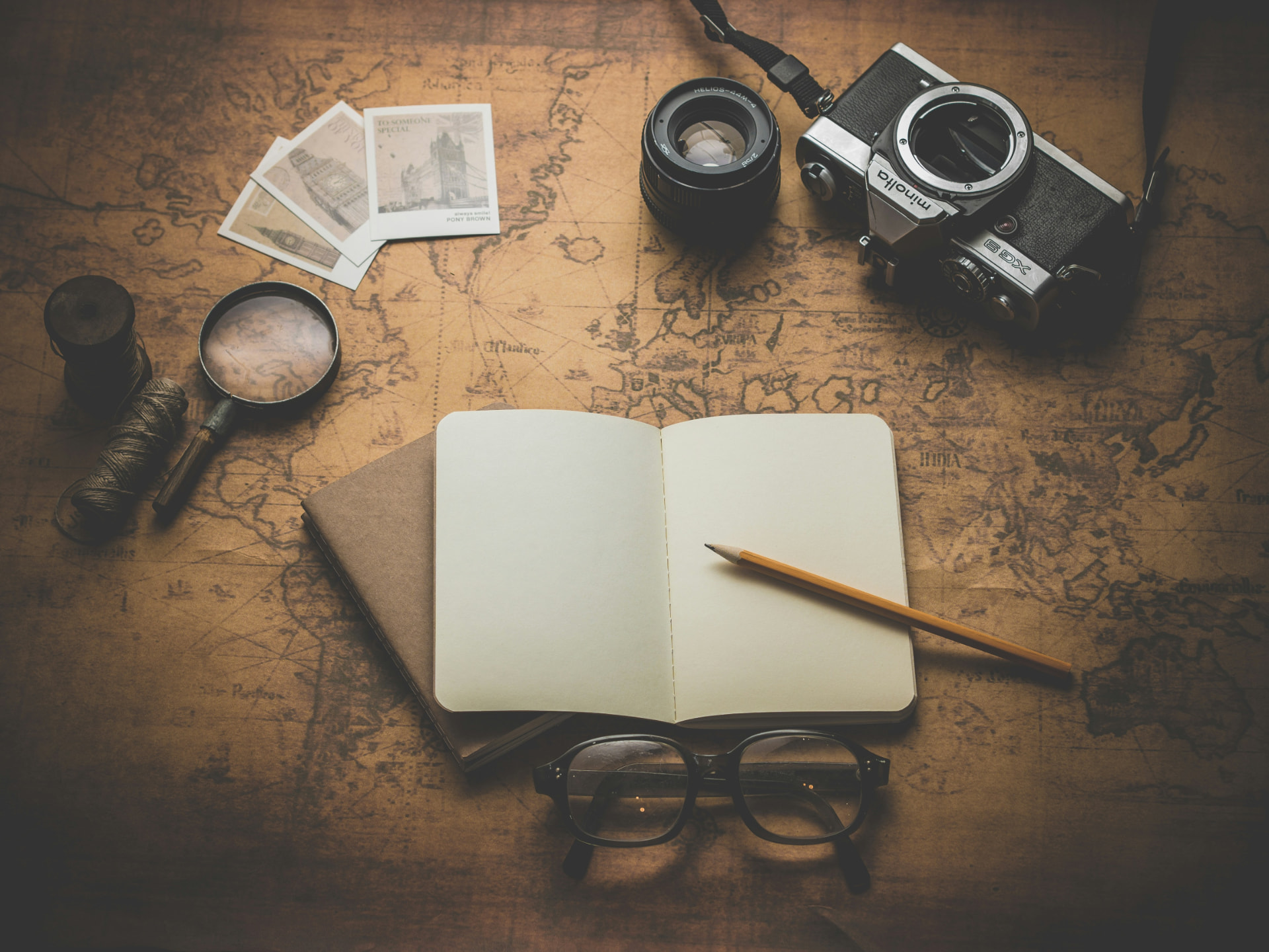 A journal, pencil, magnifier, and camera resting on an antique map